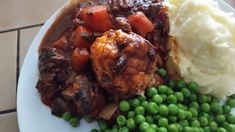 a white plate topped with meat, mashed potatoes and green peas on top of a tile floor