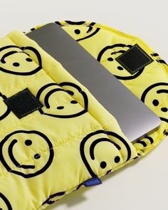 an open laptop computer sitting on top of a yellow bag with smiley faces printed on it