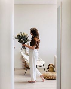 a woman is standing in the hallway with her back to the camera and holding a vase full of flowers