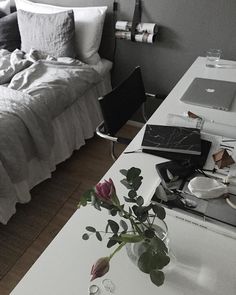 a white table topped with a glass vase filled with flowers next to a laptop computer