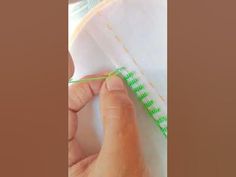 someone is stitching something with green thread on the edge of a piece of paper