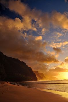 two people walking on the beach at sunset with mountains in the backgrouund