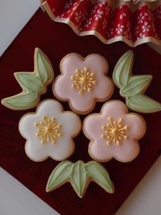 four decorated cookies sitting on top of a red tray next to a cupcake tin