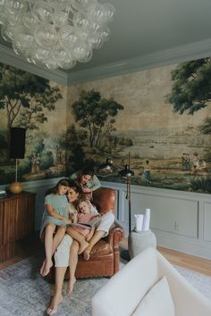 a family sitting on a couch in front of a wall with a painting behind them