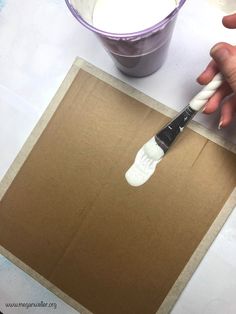 someone is using a paintbrush to paint a piece of cardboard with white paint on it