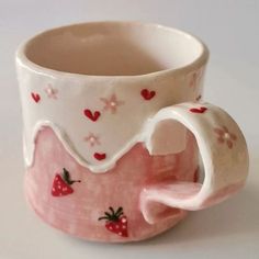 a pink and white coffee cup with strawberries painted on the side, sitting on a table