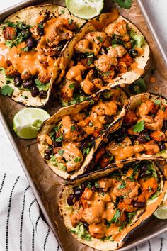 fish tacos with guacamole and lime wedges on a baking sheet