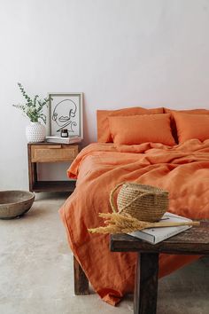 a bed with an orange comforter in a bedroom next to a wooden table and basket