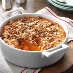 a white casserole dish filled with food on top of a wooden cutting board