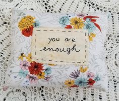 an embroidered pillow with the words you are enough written in black ink on it, sitting on a lace doily