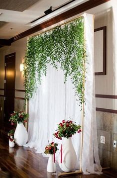 some white vases with flowers and greenery in them on a wooden floor next to a curtain