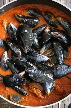 a pan filled with mussels and sauce on top of a wooden table