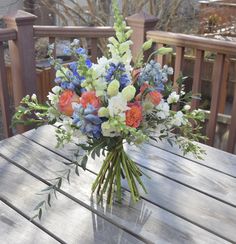 a bouquet of flowers sitting on top of a wooden table next to a railing outside