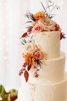 a three tiered white cake with flowers and leaves on the top is sitting on a table