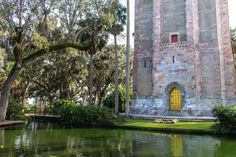 an old brick tower with a yellow door next to a body of water and trees