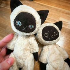 a hand holding two black and white stuffed animals on top of a wooden floor next to a person's hand