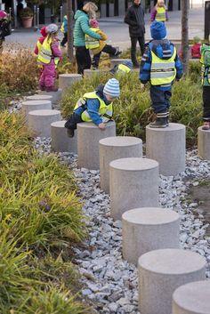 children in yellow vests are playing on cement blocks