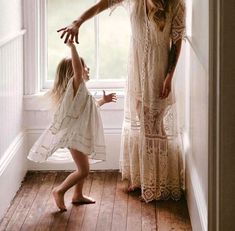 a mother and her daughter standing in front of a window with their arms stretched out