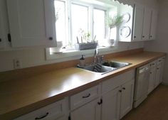 a kitchen with white cabinets and wooden counter tops, along with a window over the sink