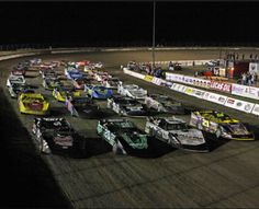 a group of cars driving around a track at night