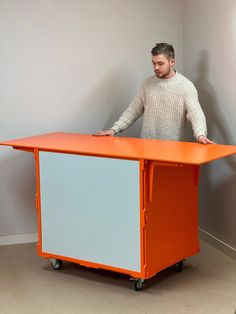 a man standing next to an orange and white desk with wheels on the bottom shelf