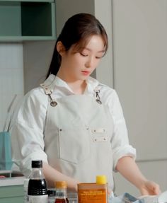 a woman in an apron preparing food on top of a kitchen counter with condiments