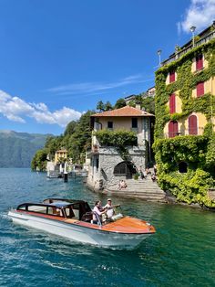 a boat traveling down a river next to a tall building with red shutters on the windows