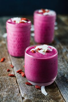 three glasses filled with pink smoothie and garnished with flower petals on wooden table