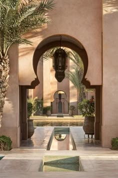 an archway leading into a courtyard with a fountain and palm trees in the foreground