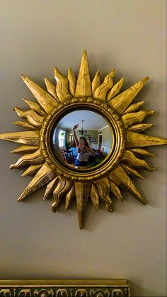 a gold sun shaped mirror mounted on the wall above a table with a person sitting in it