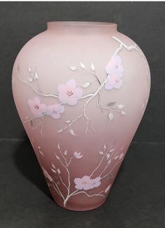 a pink vase with white flowers painted on the side and branches in the middle, sitting on a black surface