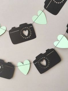 some paper hearts are hanging from a string on the wall with camera and heart cutouts