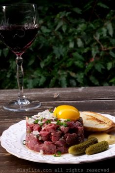 a white plate topped with meat and vegetables next to a glass of wine on top of a wooden table