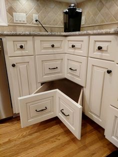 an open drawer in the middle of a kitchen countertop with white cabinets and drawers