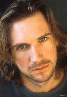 a man with long hair and blue eyes looks at the camera while wearing a black shirt