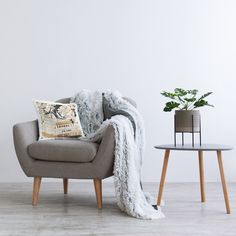 a chair with a blanket on it next to a table and potted plant in the corner