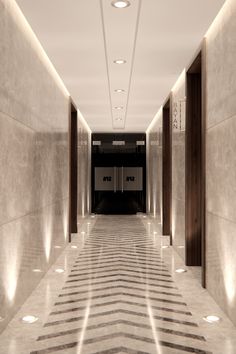 an empty hallway with marble floors and lights on either side of the corridor is lit by recessed lighting