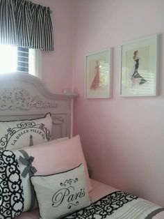 a bedroom with pink walls and black and white decor on the bed, two framed pictures above the headboard