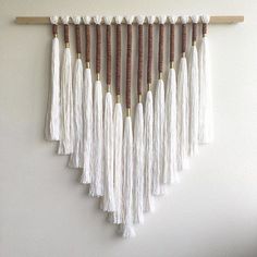 a white wall hanging with tassels and wooden pegs on the side,