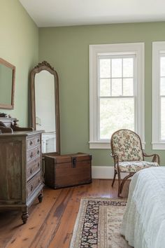 a bedroom with a bed, dresser and chair in it's corner next to two windows