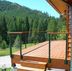 a wooden deck with green railings next to trees