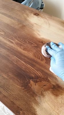 a person in blue gloves wiping up wood with a cloth on top of the table