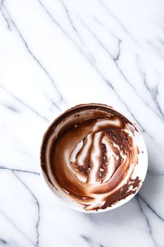 a cup filled with liquid on top of a white marble countertop covered in brown and white swirls