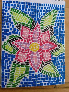 a colorful flower made out of colored paper on a wooden table with blue and green tiles