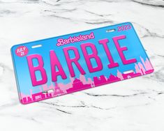 a license plate with the name barbie written in pink and blue on it, sitting on a marble surface