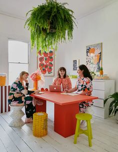 three women sitting at a table in front of a potted plant and an orange stool