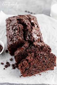 a loaf of chocolate cake sitting on top of a piece of paper next to a cup of milk