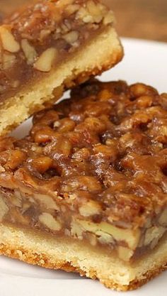 two pieces of pecan bar sitting on top of a white plate next to each other