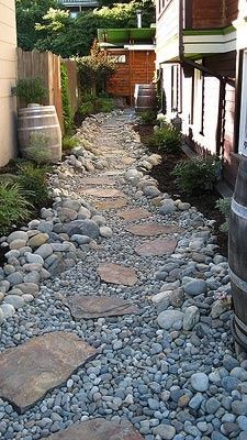 a stone path between two buildings with barrels on each side and rocks in the middle