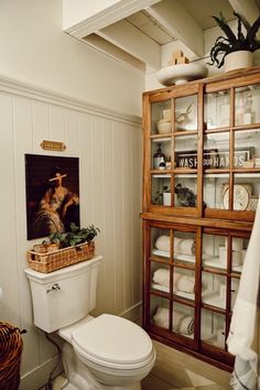 a white toilet sitting in a bathroom next to a wooden cabinet filled with dishes and towels